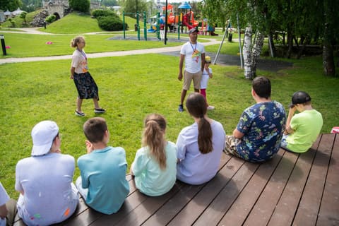 Дети сидят на деревянном настиле и смотрят игру на газоне