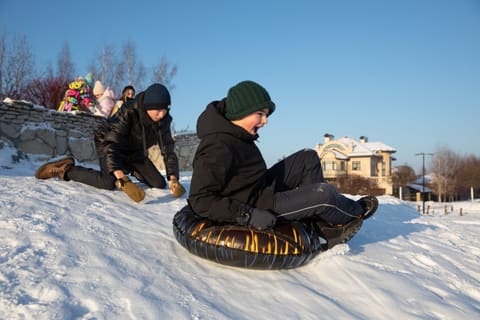 Спуск на ватрушке с горки, на заднем плане дома посёлка