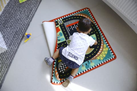 Мальчик играет с машинкой на ковре с дорогами
